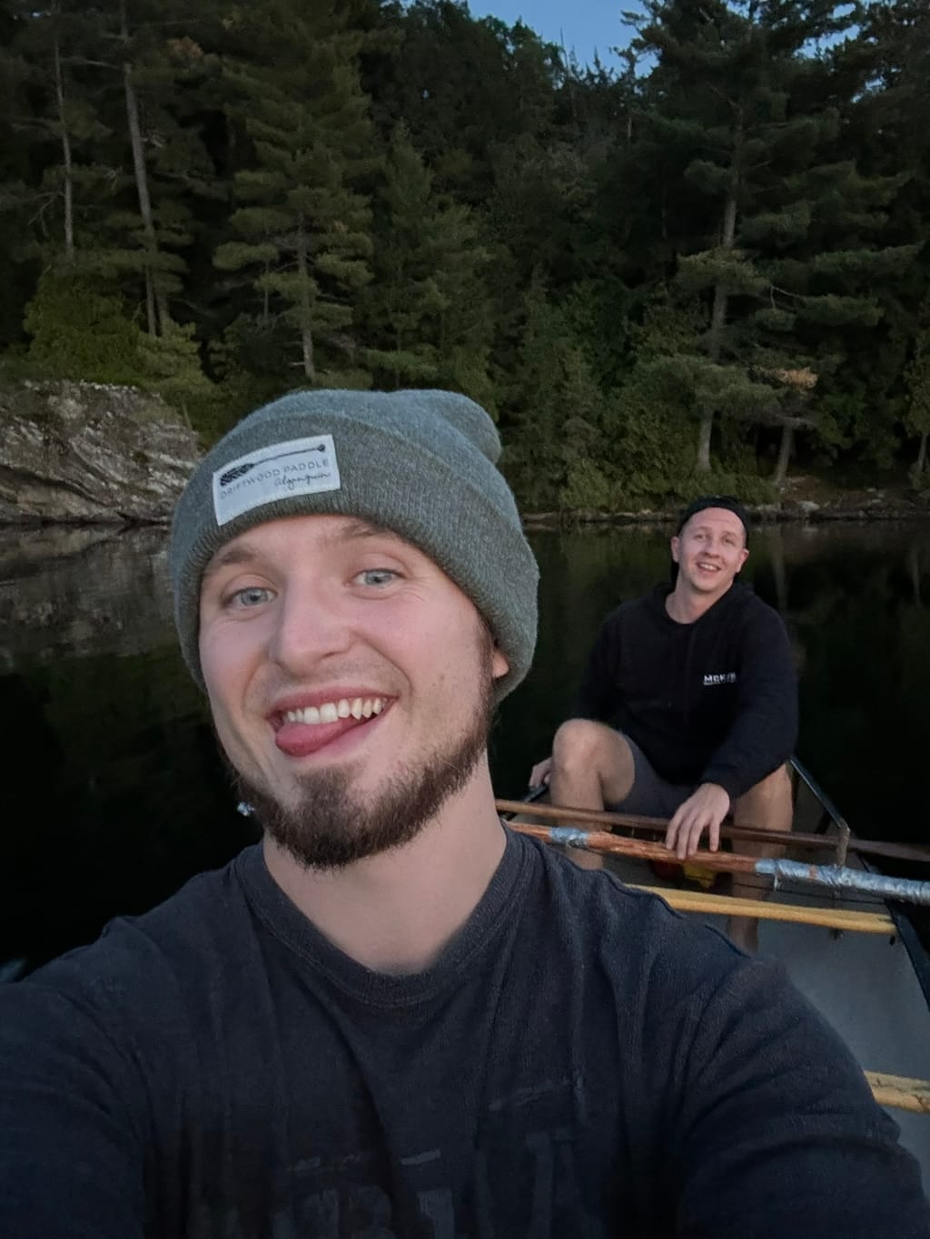 Brett and a friend paddling a canoe on a calm lake surrounded by pine trees