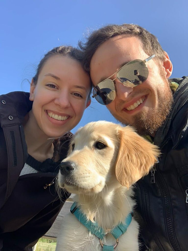 Original colour photo of two people and their golden retriever outdoors under a blue sky